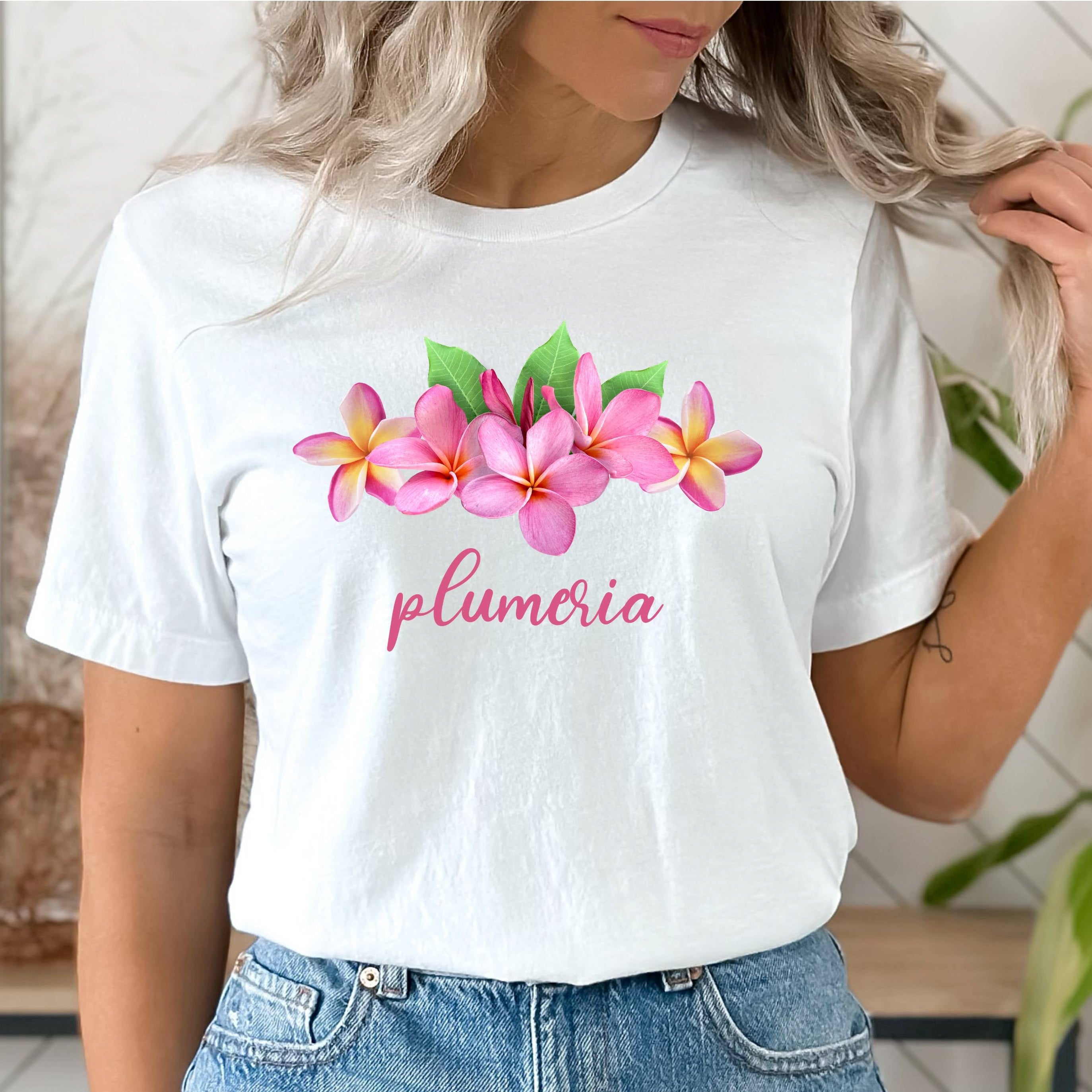 White t-shirt with pink floral design and 'plumeria' text worn by a person.